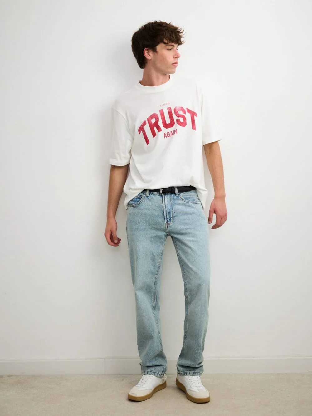דוגמן בחולצה לבנה עם הדפס TRUST AGAIN וג׳ינס בהיר